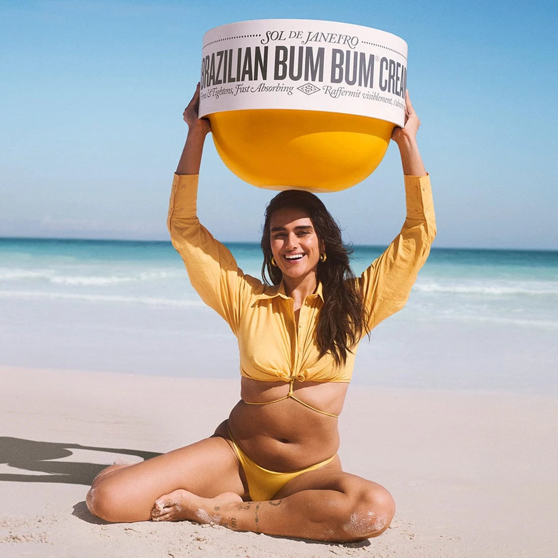 Woman holding a large container of 'Brazilian Bum Bum Cream' on a beach.